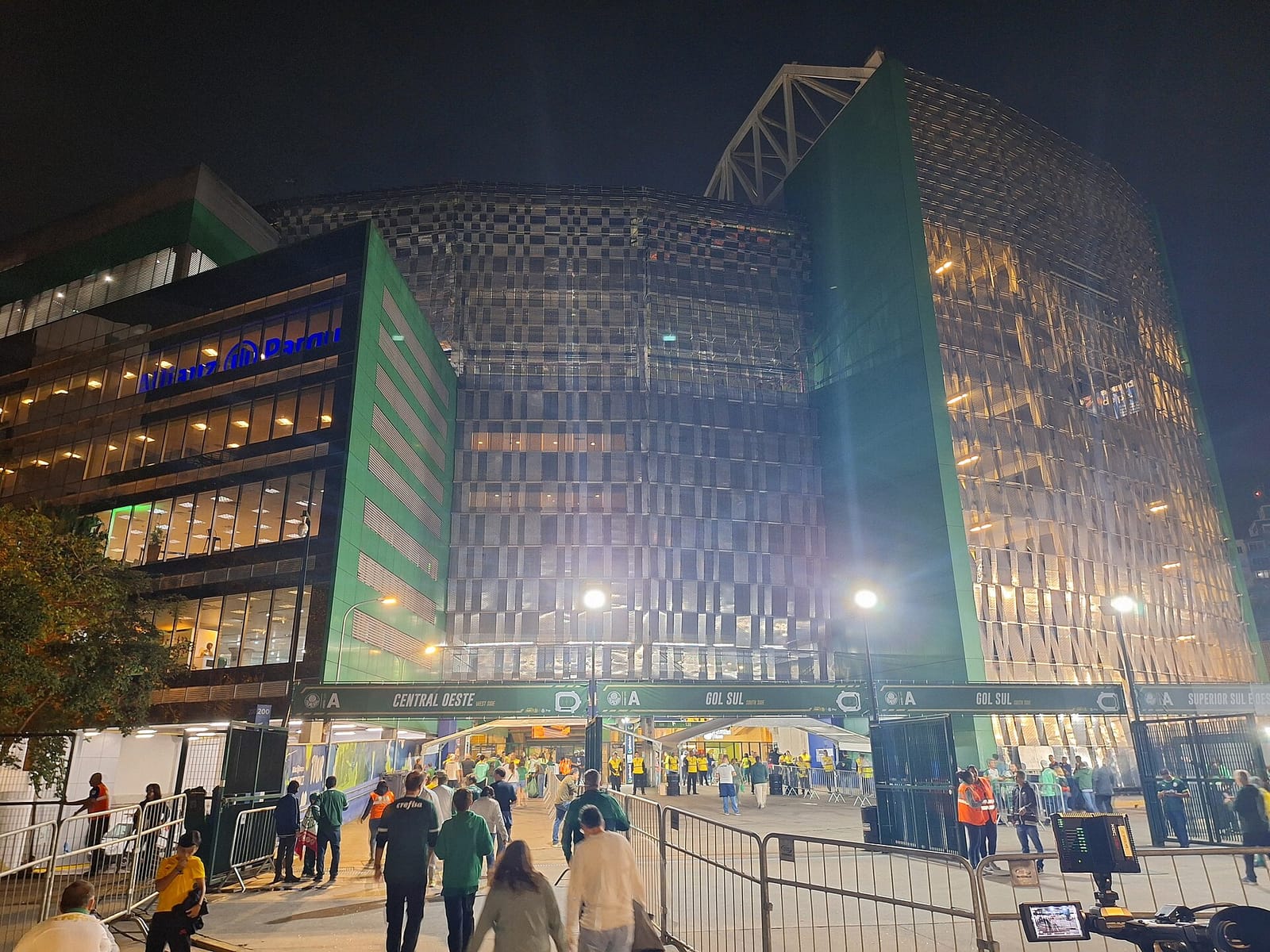 Fachada do estádio iluminada à noite, com público chegando